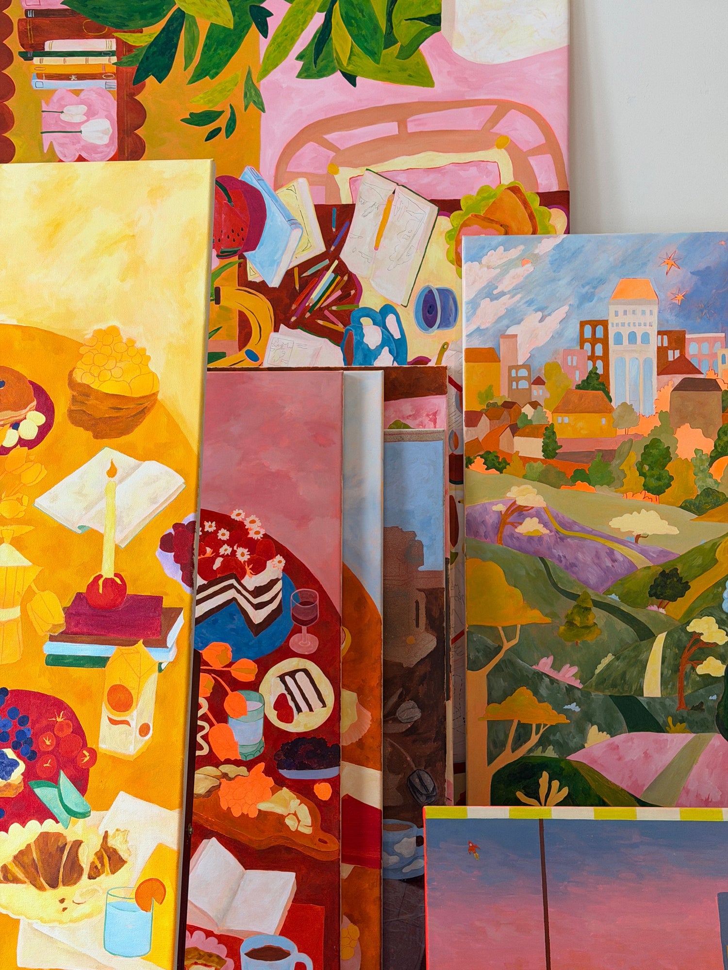 Multiple original paintings arranged in a layered stack, canvases leaning against each other and overlapping in an artist’s workspace.